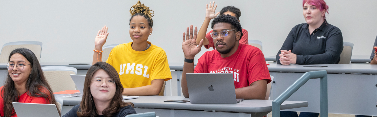 diverse umsl students raising hands in a classroom