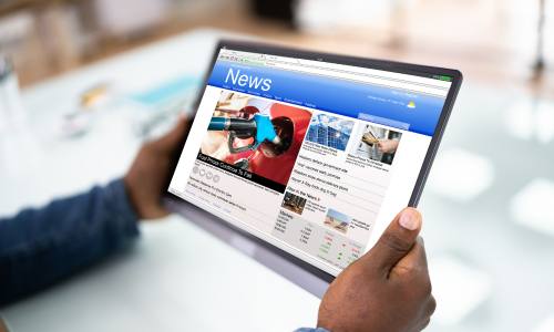 Two hands holding a tablet that displays a News website.