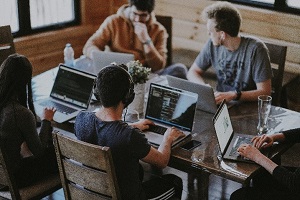 Picture of four students at table talking with computers in front of them